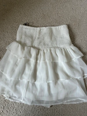 Vit volangkjol från Bik Bok - Söt vit kortkjol från Bik Bok med flera lager volanger och smockad midja! Passar nog xs-m 💕liten sminkfläck på baksidan av kjolen men kan tvättas bort 🥰