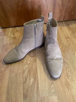 Beige stövletter i mocka med dragkedja - Snygga beige stövletter i mocka med smal tå och låg klack. Dragkedja på sidan för enkel påtagning och stilren look. Perfekta för dig som gillar en clean och trendig stil. Passar till både jeans och kjol.