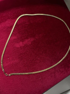 Guld planterat  - Snyggt halsband i guldton med platt kedjedesign. Halsbandet har en enkel och stilren look som passar perfekt till olika outfits. Materialet ser ut att vara metall med en blank finish. Lås med klassisk karbinhake.