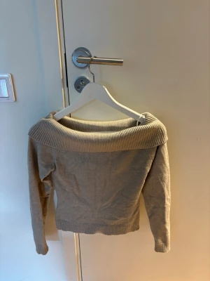 Beige off shoulder stickad tröja - Säljer en beige stickad tröja från Gina Tricot med bred off shoulder-krage och ribbade muddar. Tröjan har lång ärm och är i mjukt material, perfekt för dig som gillar en avslappnad men ändå trendig stil.