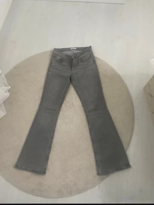 Gråa bootcut jeans - Säljer ett par gråa bootcut jeans med klassisk femficksmodell och normal midja. Jeansen har utsvängda ben och är tillverkade i ett mjukt denimtyg som ger en snygg siluett. Perfekta för dig som gillar retrovibbar och vill ha något som sticker ut.