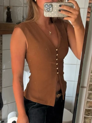 Brun väst med v-ringning och knappar - Brun väst med v-ringning och dekorativa knappar framtill i en figursydd passform🤎🤎🤎använd enbart vid ett tillfälle!