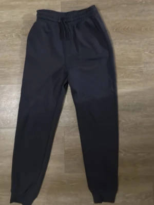 Mörkblå mjukisbyxor från H&M - Säljer ett par mörkblå mjukisbyxor från H&M med dragsko i midjan och ribbade muddar vid bensluten. Byxorna har en avslappnad passform och är tillverkade i mjukt material, perfekta för chill dagar. Klassisk look med fickor på sidorna.