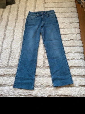Blå raka jeans med hög midja - Säljer ett par klassiska blå jeans med rak passform och hög midja. Jeansen har fem fickor, bälteshällor och stängs med knapp och dragkedja. Perfekta till vardagslooken och passar till det mesta.