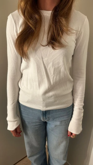 Vit långärmad tröja i bomull - Klassisk vit långärmad tröja med rund hals och ribbade muddar. Tröjan är enkel och stilren, perfekt att matcha med jeans eller kjol. Tillverkad i mjukt bomullsmaterial för en bekväm känsla.