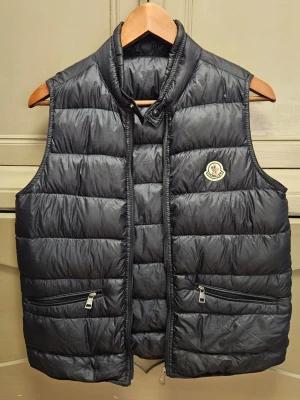 Mörkblå dunväst från Moncler - Äkta moncler gui väst. Nypris 7000. Om du har någon fråga är det bara att höra av dig. Skicket är bra utan några defekter. Storlek passar är ungefär mellan xs till small och enligt moncler passar det någon som är 14 år.