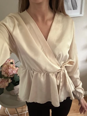 Beige omlottblus med knytband - Söt beige omlottblus med knytband i midjan ifrån Missäy💓det finns sminkfläckar (kolla 3 o 4 bilden) på insidan av tröjan därav priset men det är inget som syns när man har på sig den, så pris kan självklart diskuteras💓 är osäker på storleken men den passar mig som har xs så skulle gissa att den är en xs-s💓