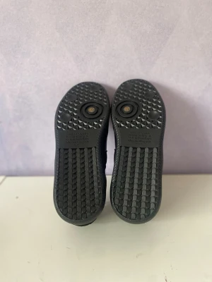 Maison Margiela svarta sneakers - Maison Margiela sneakers i svart mocka och läder med klassisk låg siluett. Skorna har svarta snören, gummisula med unikt mönster och diskreta detaljer. Perfekta för dig som gillar stilrena och exklusiva sneakers.