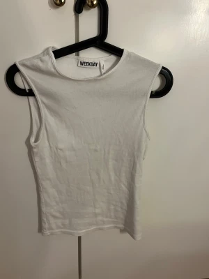 Vit ribbad ärmlös topp Weekday - Säljer en vit ribbad ärmlös topp från Weekday. Toppen har rund halsringning och är tillverkad i ett stretchigt material som sitter snyggt på kroppen. Perfekt att styla med jeans eller kjol för en clean look.