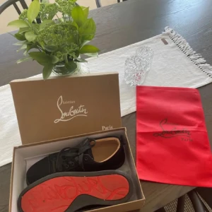 Christian Louboutin  - Snygga svarta sneakers från Christian Louboutin i mocka med klassisk röd sula och svarta snören. Skorna har rund tå och platt sula, samt diskreta detaljer som gör dem riktigt stilrena. Perfekta för dig som vill sticka ut med exklusiva skor. Dem är smått använda, därmed det låga priset.