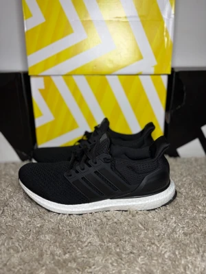  Adidas Ultraboost  - Snygga svarta Adidas Ultraboost sneakers med stickad ovandel i mesh och klassiska tre ränder på sidan. Skorna har en vit, dämpande Boost-sula och svart yttersula. Perfekta för dig som gillar sportig och modern stil.