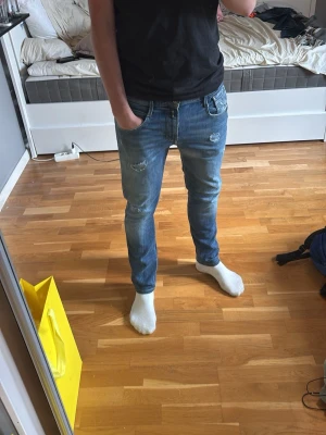 Slim fit blå jeans med slitningar - Säljer ett par slim fit blå jeans med snygga slitningar på låren och knäna. Jeansen har klassisk femficksdesign och är tillverkade i stretchigt denimtyg för skön passform. Perfekta för en avslappnad och trendig look.