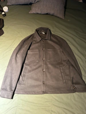 Overshirt från Zara  - Stilren grön overshirt med klassisk krage och knäppning framtill. Två stora bröstfickor och två sidofickor ger en clean look. Materialet är i mocka, perfekt för lager-på-lager. Passar dig som gillar minimalistisk stil.