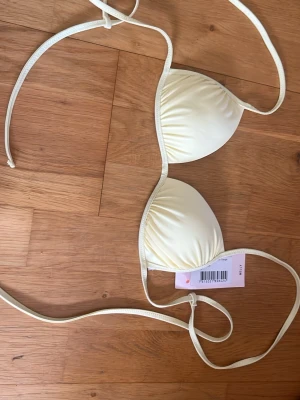 Ljusgul triangelbikini från Nelly - Säljer en ljusgul triangelbikini från Nelly med tunna knytband och lätt vadderade kupor. Perfekt för soliga dagar på stranden eller vid poolen. Enkel och stilren design som ger en fräsch sommarkänsla.