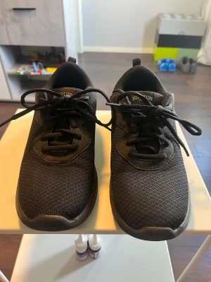 Svarta mesh sneakers med snörning - Snygga helsvarta sneakers med ovandel i mesh-tyg och klassisk snörning. Skorna har en låg profil och en bekväm, vadderad kant runt ankeln. Perfekta för dig som gillar en stilren och enkel look.