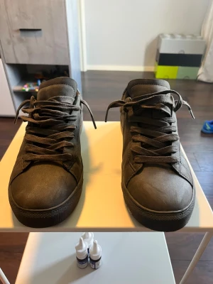 Mörkbruna låga sneakers i mocka - Säljer ett par stilrena mörkbruna sneakers i mocka-look med matchande snörning och diskreta sömmar. Skorna har en klassisk låg profil och en robust gummisula. Perfekta för dig som gillar en clean och enkel stil.
