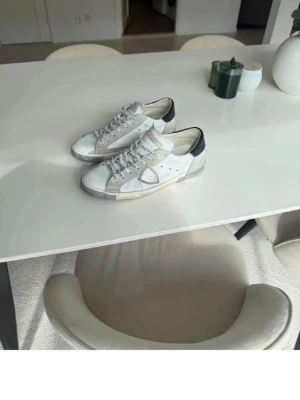 Vita sneakers med svart detalj - Snygga vita sneakers med svarta detaljer på hälen och grå inslag. Klassisk låg modell med snörning och perforerade sidor. Passar perfekt till streetwear och casual outfits.