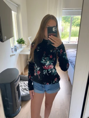 Svart tröja med blommigt mönster - Snygg svart sammet tröja med färgglatt blommigt mönster i rosa, grönt och vitt. Tröjan har rund halsringning och långa ärmar. Perfekt för dig som vill ha en trendig och bekväm stil med lite extra färg.
