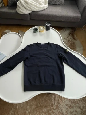 Mörkblå sweatshirt från Stone Island - Snygg mörkblå sweatshirt från Stone Island med klassisk rund hals och ikonisk patch på vänster ärm. Tröjan är tillverkad i mjuk 100% bomull och har ribbade muddar vid ärmslut och nederkant. Perfekt för en clean och stilren look. Storlek 12år/156 