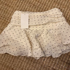 Vit prickig volangkjol från Zara, helt ny!  - Supersöt kort kjol från Zara med prickar och volangdetaljer. Kjolen har inbyggda shorts och dragkedja i sidan! Ny med prislapp kvar 