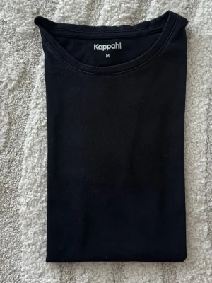 Svart t-shirt från Kappahl - En klassisk svart t-shirt från Kappahl i storlek M. T-shirten har rund halsringning och är tillverkad i mjuk bomull. Perfekt basplagg som passar till allt och är enkel att styla.