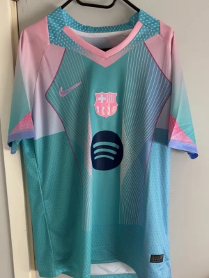 Barcelona Lamine Yamal matchtröja - Snygg Barcelona matchtröja i turkos, rosa och lila med vita detaljer. Tröjan har tryck med Lamine Yamal och nummer 10 på ryggen, samt klubbmärke och sponsorlogga på bröstet. Perfekt för fotboll eller träning.