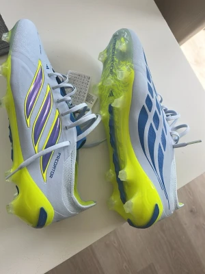 Adidas Predator fotbollsskor Helt Nya‼️ - Snygga Adidas Predator fotbollsskor i ljusblått med neon-gula och blå detaljer. Skorna har klassisk snörning, låg profil och mönstrad sula för bra grepp på planen. Tillverkade i syntetmaterial för lätt känsla och bra bollkontroll. Kan få påse till 