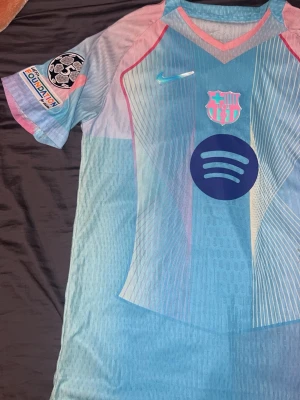 Barça Nike matchtröja blå/rosa - Säljer en FC Barcelona matchtröja från Nike i ljusblått med rosa och vita detaljer. Tröjan har klubbmärke, Nike-logga och Spotify som sponsortryck på bröstet samt Champions League-märke på ärmen. Perfekt för dig som älskar fotboll och vill sticka ut på planen.