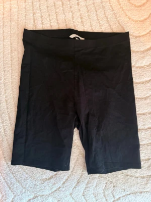Svarta cykelshorts i bomull - Säljer ett par svarta cykelshorts i mjuk bomull. De har en enkel, tight passform och är perfekta till sommaren. Midjan är elastisk och shortsen är utan synliga detaljer eller fickor.