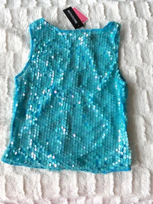 Blå paljettopp från PrettyLittleThing - Säljer en glittrig blå paljettopp från PrettyLittleThing. Toppen är ärmlös, croppad och har dragkedja i ryggen. Perfekt för dig som vill sticka ut med en färgstark och festlig look. Passar till alla som älskar att glänsa!