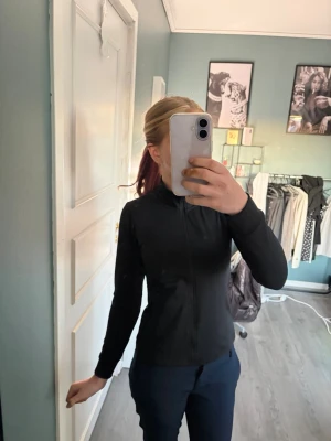 Svart träningsjacka med dragkedja - Svart sportjacka från SOC med hel dragkedja och hög krage. Tröjan har långa ärmar, två sidofickor med dragkedja och en liten vit logga på ryggen. Materialet är lätt och smidigt, perfekt för träning och utomhusaktiviteter. Använd fåtal gånger. Säljer för att den är för liten, pris går att diskutera🫶🏻
