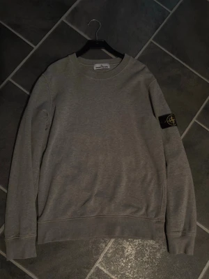 Grå sweatshirt från Stone Island - Säljer denna Stone Island tröja då den är för liten. Köpt från Man of a kind. Fint skick och självklart äkta✅ Passar även M
