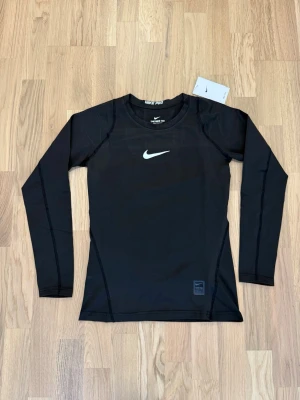 Nike pro träningströja - Snygg svart långärmad träningströja från Nike med vit logga på bröstet. Storlek M men kan passa S-M beror på kroppen.  Tillverkad i ett stretchigt funktionsmaterial som andas, perfekt för träningspass.