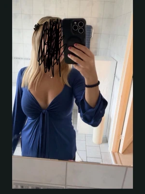 Marinblå långärmad topp med knyt - Snygg marinblå topp med djup v-ringning och knyt framtill. Långärmad modell i mjukt, stretchigt material som ger en smickrande passform. Perfekt för dig som vill ha en stilren men ändå trendig look.