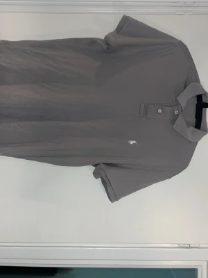 Grå pikéskjorta från Polo Ralph Lauren - Säljer en grå pikéskjorta från Polo Ralph Lauren med klassisk krage, två knappar vid halsen och liten vit broderad logga på bröstet. Skjortan är gjord i mjuk bomull och är i storlek M regular fit. Pris kan diskuteras.