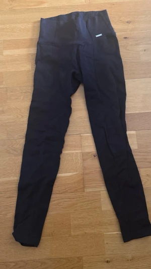 Svarta leggings med hög midja aim’n - Säljer ett par svarta leggings med hög midja och diskret struktur i tyget. De har en tight passform och långa ben, perfekta för en sportig och trendig look. Materialet ser ut att vara stretchigt och bekvämt.