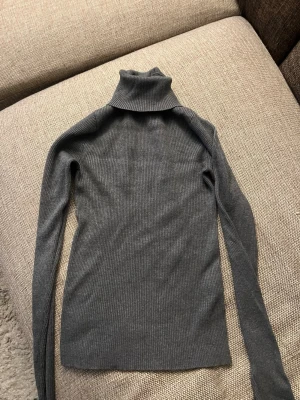 Mörkgrå polotröja från Gina Tricot - Säljer en mörkgrå, ribbstickad polotröja från Gina Tricot i storlek M. Tröjan har lång ärm, smal passform och hög polokrage. Perfekt att styla med jeans eller kjol för en clean och enkel look.