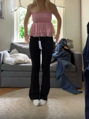 Rosa bandeau topp med volanger - Supersöt rosa bandeau topp med smockad överdel och dubbla volanglager nedtill. Toppen är axelbandslös och har en luftig, flowy känsla som passar perfekt till jeans eller kjol. Materialet känns lätt och somrigt. Använd sällan och i stl xs! 