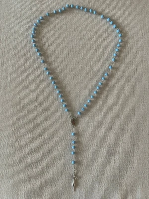 Blått rosenkranshalsband med pärlor - Halsband med ljusblå runda pärlor och silverfärgade detaljer. Halsbandet har ett kors och en medaljong i metall, vilket ger en klassisk och stilren vibe. Perfekt för dig som gillar smycken med religiösa inslag och unik design.