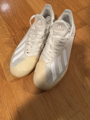 Vita Adidas fotbollsskor med gummisula - Säljer ett par vita Adidas fotbollsskor med klassiska tre ränder på sidan. Skorna har ovandel i mesh och syntetmaterial för bra ventilation och komfort. Yttersulan är i gummi, perfekt för spel på inomhusplaner. Snygg och sportig design som sticker ut på planen.