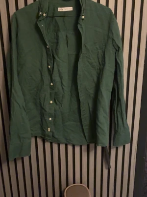 Grön linneskjorta från Zara - Snygg grön skjorta från Zara i linne. Skjortan har klassisk krage, långa ärmar och vita knappar framtill. Perfekt för dig som gillar en avslappnad men ändå stilren look.