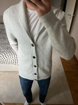 Ljusgrå kofta med knappar - Säljer en sjukt fet stickad cardigan från Hollister gjord i ett väldigt skönt material. Cardiganen är i ett väldigt fint skick utan defekter! ✌🏼——————————————————————————                                                                      📐| Storlek: L                                                           👖| Märke: Hollister                                                🔎| Skick: Mycket Fint!                                                     ✍🏻| Skriv om du har några frågor