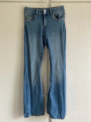Blå bootcut jeans med nitar - Snygga ljusblå bootcut jeans med högre midja. Jeansen har dekorativa nitar på ficklocken och dubbla knappar i midjan. Klassisk femficksmodell i mjuk denim med cool tvätt. Bra skick!💞