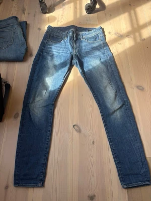 Blå slim fit jeans med slitningar - Snygga blå slim fit jeans med lätt slitna detaljer och klassisk femficksdesign. Jeansen har en smal passform och är tillverkade i ett mjukt denimtyg som ger en bekväm känsla. Perfekta för en avslappnad och trendig stil. Storlek 31/32