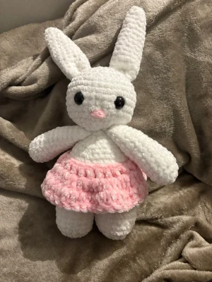 Virkad kanin i rosa kjol - Supergullig handvirkad kanin i mjukt vitt garn med stora svarta ögon och rosa nos. Kaninen har en fluffig rosa kjol och långa öron. Perfekt som present eller dekoration. Gjord av mjukt garn för extra mysfaktor.