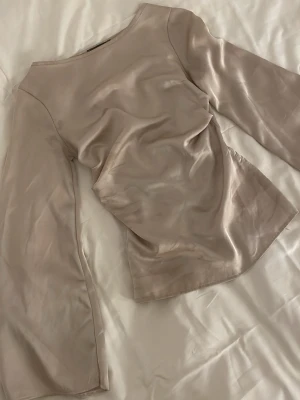 Champagnefärgad långärmad satintopp - Snygg långärmad topp i champagnefärgat satinmaterial med rund halsringning. Toppen har en slät och glansig yta som ger en lyxig känsla och är perfekt att styla till olika outfits.