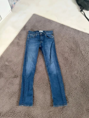 Blå skinny jeans från Replay - Snygga blå skinny jeans från Replay Sustainable Lab med klassisk femficksdesign och dragkedjegylf. Jeansen har en tvättad look och smal passform som sitter tajt längs benen. Perfekta för dig som gillar en stilren och modern vibe.