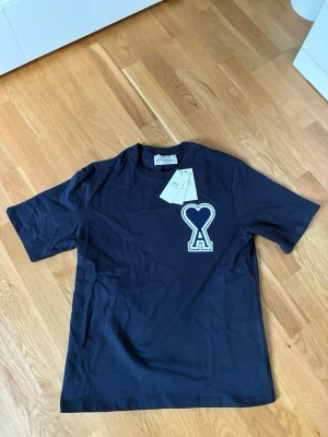 Ami Paris t-shirt  - Snygg marinblå t-shirt från Ami Paris med det ikoniska hjärta-A broderiet på bröstet. Tillverkad i mjuk bomull och har en klassisk passform med korta ärmar och rund hals. Perfekt för en clean och stilren look.