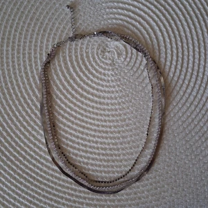 Treradigt silverfärgat halsband - Treradigt halsband med en ormlänkskesja, en strasskedkja och kulpärlformadkedja. Halsbandet har ett justerbart lås. Längd ca 39 till 48 cm. Nytt och oanvänd men saknar föepackning och prislapp.