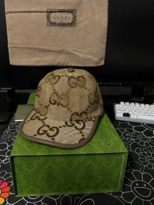 Beige keps med mönster - Snygg beige keps med det klassiska monogrammet i brunt över hela kepsen. Kepsen har böjd skärm och är tillverkad i ett canvasliknande material. Perfekt accessoar för att lyfta din outfit med en lyxig touch.box ingår inte bara kepsen 